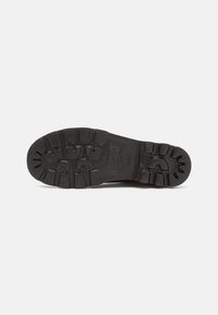 Semelle d'une botte noire robuste avec des motifs de semelle profonds et le nom de la marque embossé sur la zone de la voûte plantaire sur un fond uni.