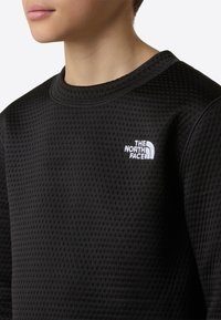 Čierna mikina s textúrovaným vzorom, okrúhlym výstrihom a bielym vyšitým logom "The North Face" na ľavej strane hrudníka.