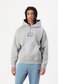 Šedá bavlněná mikina s kapucí, přední kapsou a modrým grafickým logem. Kombinováno se světle modrými sportovními kalhotami s logem Nike.