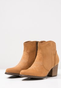 Botas de tobillo marrones de ante, con un acabado texturizado, cremallera lateral y costuras decorativas en la parte delantera. Diseño de tacón cuadrado.