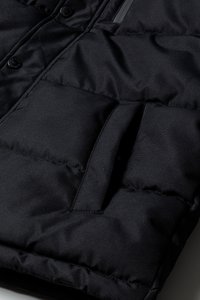 Pochetto di una giacca nera trapuntata con apertura verticale e linee di cucitura visibili su un tessuto imbottito spesso.