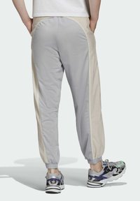 Pelēkās un bēšās sportiskās bikses ar elastīgām piekaklēm un sānu kabatām, ar gludu tekstūru un sportisku dizainu, papildinātas ar daudzkrāsainām sporta kurpēm.