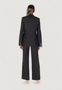 Completo nero su misura con blazer decorato con pizzi sulle maniche e pantaloni a gamba larga. Tessuto morbido con una vestibilità strutturata.