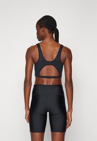 Top desportivo preto com um design em U nas costas e tecido texturizado, combinado com calções de ciclismo pretos de cintura alta, ambos com um acabamento suave.