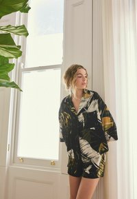 Conjunto de pantalones cortos y camisa con patrón en blanco y negro y detalles dorados. Tejido ligero, corte holgado y mangas cortas, diseñado para ofrecer comodidad.