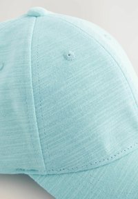 Ljusblå basebollkeps av texturerad tyg, har en rund skärm, små sömnadsdetaljer och en accent i form av en knapp på toppen.