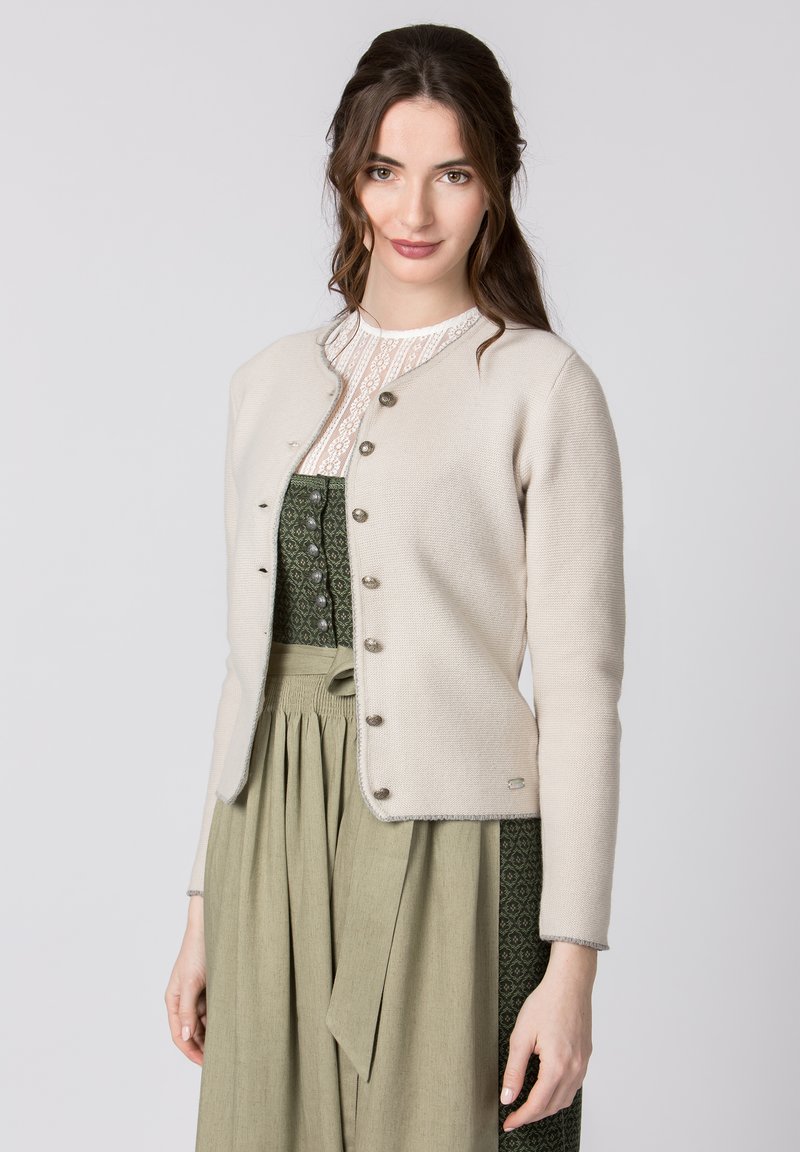 Cremfarbener Cardigan mit rundem Ausschnitt, Knopfverschluss, geripptem Textur und kontrastierenden Details. Über einem grünen, gemusterten Kleid getragen.