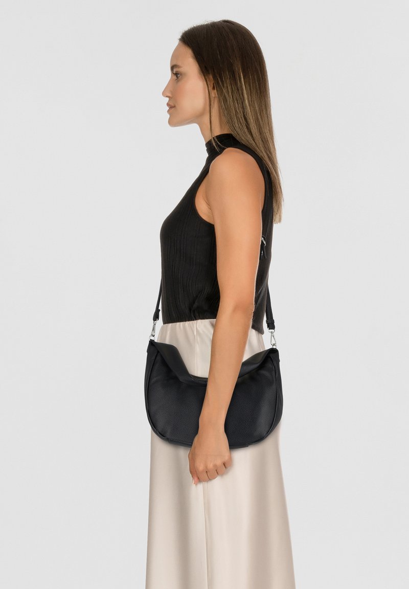 Borsa a spalla in pelle nera con un design curvo, caratterizzata da una superficie texturizzata e una tracolla regolabile. Indossata insieme a una gonna di satin chiaro.