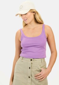Lilla bomulds tanktop med brede stropper, parret med en khaki nederdel med knaplukning foran. En beige kasket akkompagnerer outfittet.