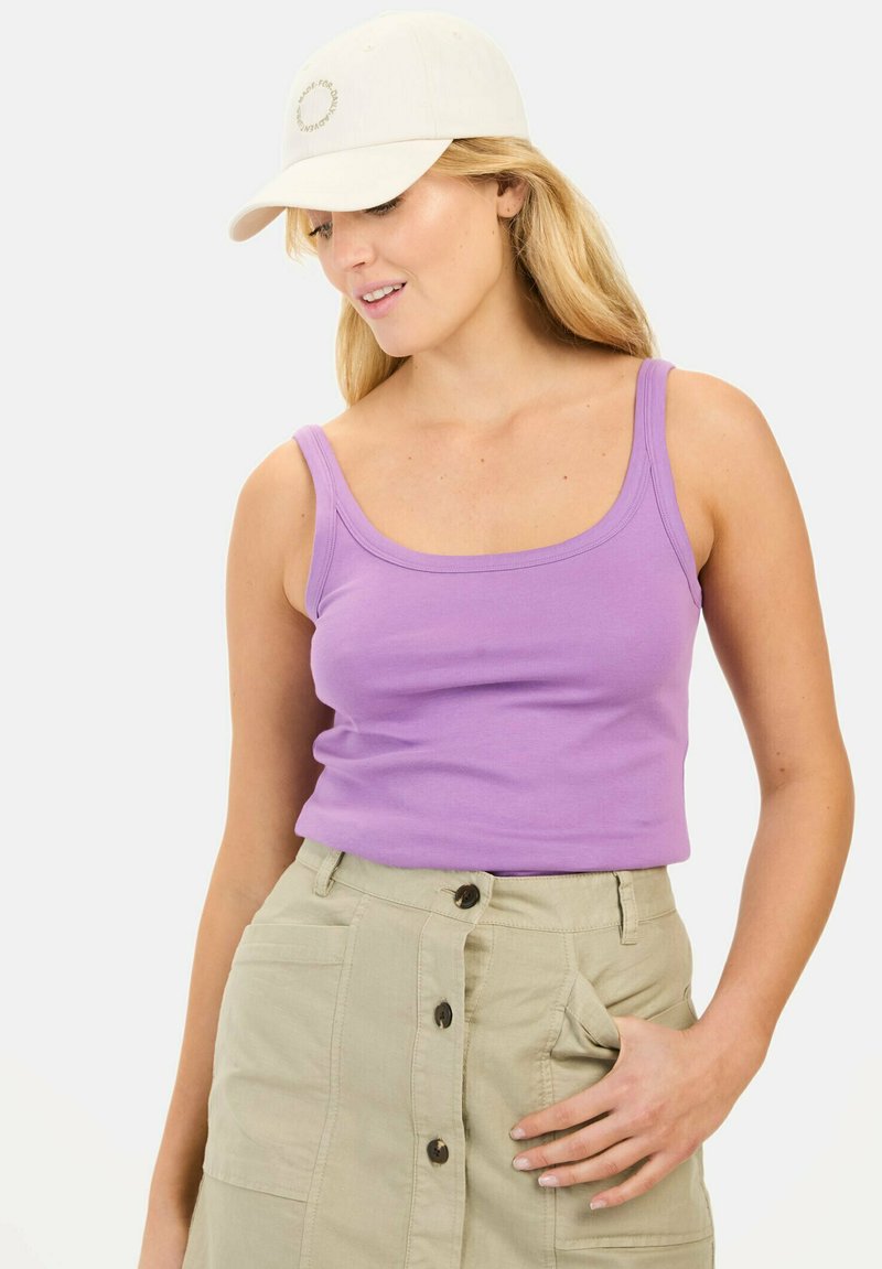 Lilla bomulds tanktop med brede stropper, parret med en khaki nederdel med knaplukning foran. En beige kasket akkompagnerer outfittet.