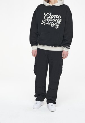 Black hoodie with white text "Came Long A Way," paired with black cargo pants. White sneakers; textured fabric, relaxed fit.