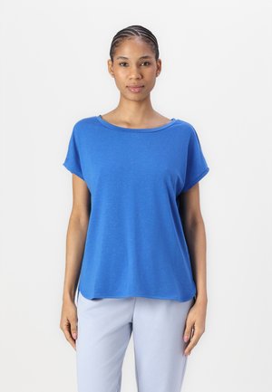 T-shirt azzurra a maniche corte realizzata in materiale morbido, caratterizzata da un colletto rotondo e una vestibilità rilassata con orlo curvo. Abbinata a pantaloni grigi chiari.