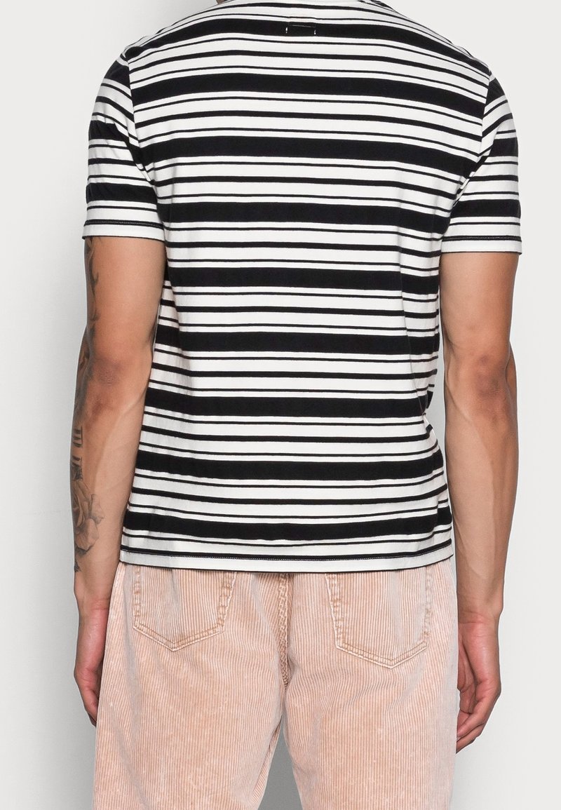 T-shirt à manches courtes rayé noir et blanc en coton, avec un col rond et une coupe ajustée, associé à un pantalon en velours côtelé rose rayé.