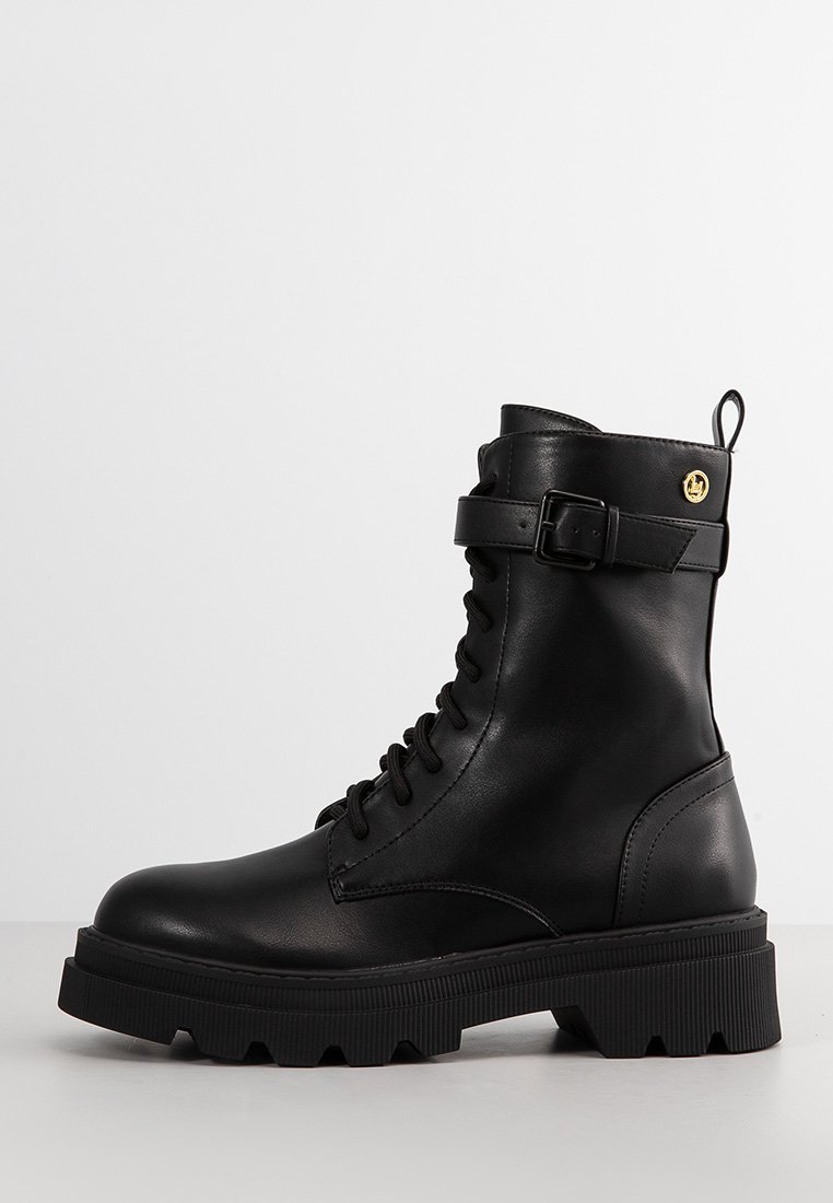 Stivaletto in pelle nera con lacci davanti, cinturino regolabile, suola in gomma resistente e dettaglio del logo dorato sul lato.