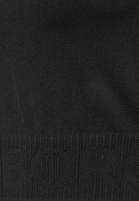 Tejido de punto negro con patrones geométricos texturizados y detalle de dobladillo acanalado.