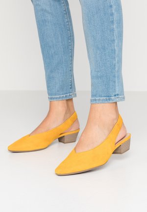Yellow suede slingback shoes with a pointed toe and a textured, stacked block heel. An open back design showcases the foot.