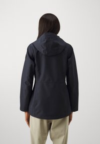 Veste imperméable bleu marine foncé avec capuche, présentant une coupe ajustée, des manches longues et une texture lisse. Aucune motif visible ni accent en métal.