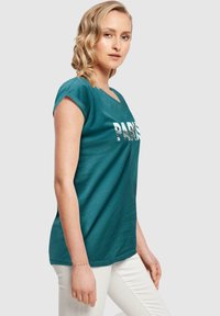 T-Shirt aus Baumwolle in Türkis mit entspanntem Schnitt, kurzen Ärmeln und rundem Halsausschnitt, versehen mit einem weißen Grafikdruck "PARIS" auf der Brust.