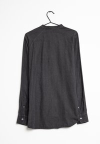 Maglietta a maniche lunghe grigio scuro con collo a camicia, polsini abbottonati e una texture liscia. Appesa a un gancio nero su uno sfondo bianco.