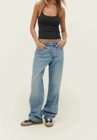 Ljust blå vida jeans i denim, med hög midja, två framfickor och knappslutning. Matchas med svarta sneakers.