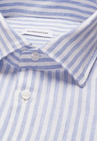 Col de chemise rayé bleu et blanc avec boutons blancs et une étiquette en tissu visible à l'intérieur du col.