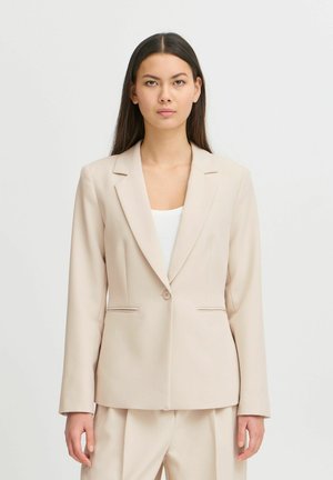 Béžový přizpůsobený blazer s jedním knoflíkem, klopovými límci a postranními kapsami. Hladká textura a přiléhavý design doplňující bílý top.