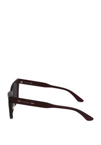 Occhiali da sole Calvin Klein in bordeaux con montatura in acetato lucido. Presentano aste spesse con logo inciso e lenti scure. Struttura robusta.