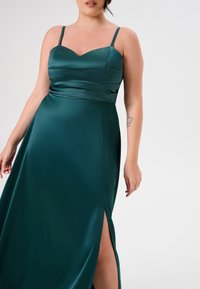 Satin-Kleid in smaragdgrün mit Herz-Ausschnitt, dünnen Trägern und seitlichem Schlitz. Glatte Textur und fließendes Design.