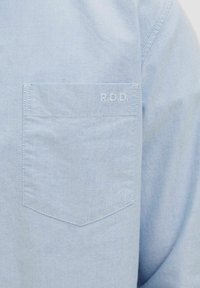 Camicia button-up azzurra chiara con taschino sul petto con le iniziali "R.D.D." ricamate in bianco. Realizzata in un tessuto testurizzato.
