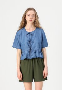 Svetlo modra denim srajca s kratkimi rokavi, peplum rob in sprednje vezanje; v kombinaciji s temno zelenimi, ohlapnimi kratkimi hlačami. Preprost dizajn.