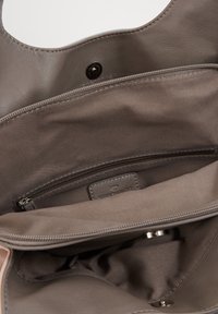 Interieur einer grauen Ledertasche mit einem Reißverschlussfach, weichem Stofffutter und einem metallenen Druckknopfverschluss, an dem ein Markenetikett sichtbar ist.