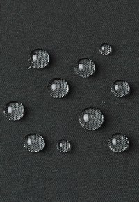Wassertropfen perlen auf einem dunkelgrauen, strukturierten Stoff und zeigen die wasserabweisenden Eigenschaften des Materials.