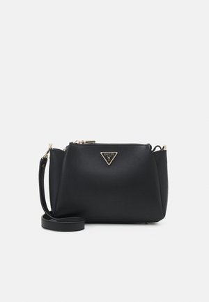 Sac bandoulière Guess noir avec logo doré et fermeture éclair, sangle réglable et forme rectangulaire structurée sur fond blanc.
