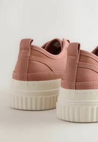 Rausvos drobinės sportbačiai su storu baltu guminiu padu, turintys tekstūruotus akcentus ir apvalų nugaros dizainą. Minimalistinio stiliaus su elastingu įėjimu.