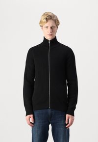 Svart ribbet zip-up genser med høy krage, med lange ermer og en tettsittende design, parret med blå jeans.