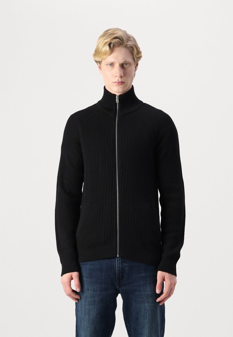 Svart ribbet zip-up genser med høy krage, med lange ermer og en tettsittende design, parret med blå jeans.