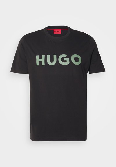 Черен памучен T-shirt с голям, смел, зелен логотип "HUGO" в централната част. Класическо кръгло деколте и къси ръкави. Обикновен фон.
