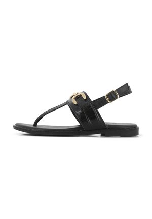 Sandalia de cuero negro con suela plana, detalle de hebilla dorada y diseño de tiras que presenta un estilo de barra T. Textura suave y diseño minimalista.