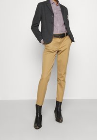 Blazer gris con botones, camiseta de rayas, pantalones beiges y botas de tobillo negras con puntas afiladas y acentos metálicos. Silueta ajustada.