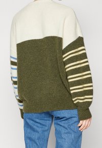 Zielony i kremowy sweter z paskowanymi rękawami, z okrągłym dekoltem, luźnym krojem i miękką teksturą. Widok z tyłu pokazuje detale w blokach kolorowych.