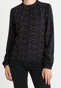 Blusa scura con collo alto e maniche lunghe, impreziosita da un motivo floreale in rosso, giallo e blu su uno sfondo nero.