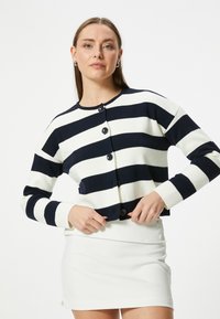Sweter w paski w kolorze granatowym i kremowym, z okrągłym dekoltem i pięcioma guzikami z przodu. Dzianinowa struktura z długimi, dopasowanymi rękawami.