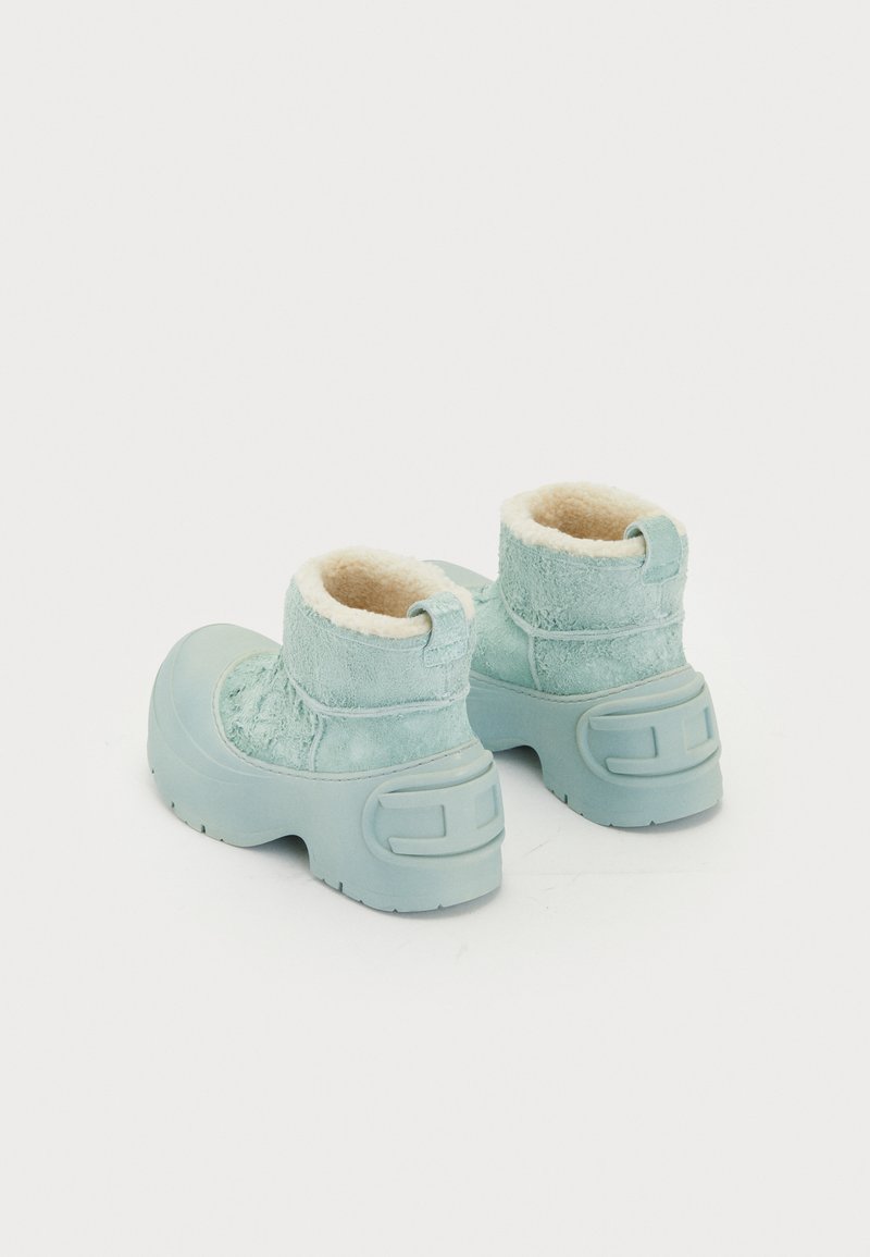 Hellblaue Plateau-Ankle-Boots mit plüschiger cremefarbener Fütterung und strukturiertem Wildleder-Obermaterial, von hinten auf weißem Hintergrund gezeigt.