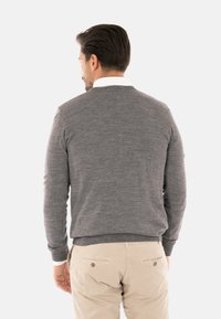 Maglione grigio con scollo rotondo e maniche lunghe, realizzato in un tessuto a maglia. Indossato sopra una camicia bianca con colletto, con cuciture visibili e polsini a costine.
