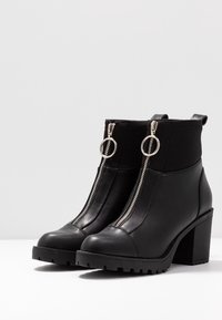 Schwarze Knöchelstiefel aus Leder mit doppeltem Reißverschluss, silbernen Hardware-Akzenten, robustem Blockabsatz und strukturiertem Gummisohle.