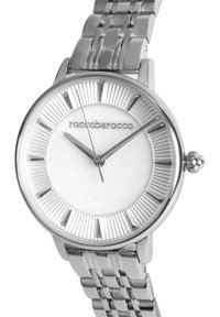 Silverfärgad metallklocka med en texturerad vit urtavla, radiella mönster och en länkarmband. Har minimalistiska timmarkörer och smala visare.