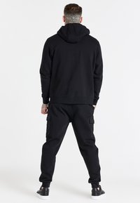 Black hoodie and cargo pants set, made of cotton. Features ribbed cuffs, kangaroo pocket, and side cargo pockets. Smooth texture and relaxed fit.
