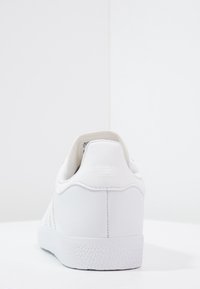 Vit lädersneaker med strukturerad sula och slät ovandel. Har en låg design och mjuk innersula. Baksidan visar minimal varumärkesinformation.