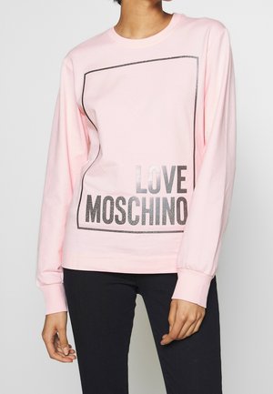 Personne portant un t-shirt rose clair à manches longues avec un carré contour noir et le texte "LOVE MOSCHINO" en grandes lettres sur le devant.