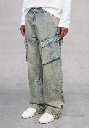 Pantalones cargo de denim azul claro, holgados, con múltiples bolsillos, costuras visibles y una textura deslavada. Combinados con zapatillas blancas.